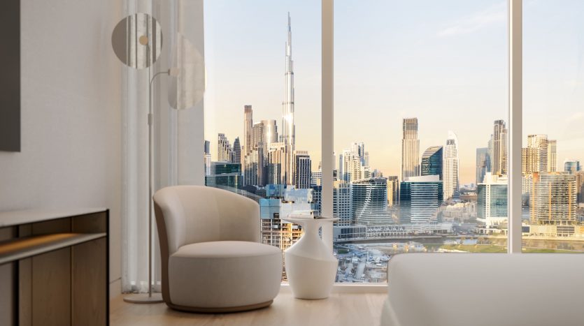 Salon moderne dans un appartement de Dubaï au décor minimaliste, comprenant deux chaises blanches et un canapé, donnant sur les toits de la ville à travers de grandes fenêtres au coucher du soleil.