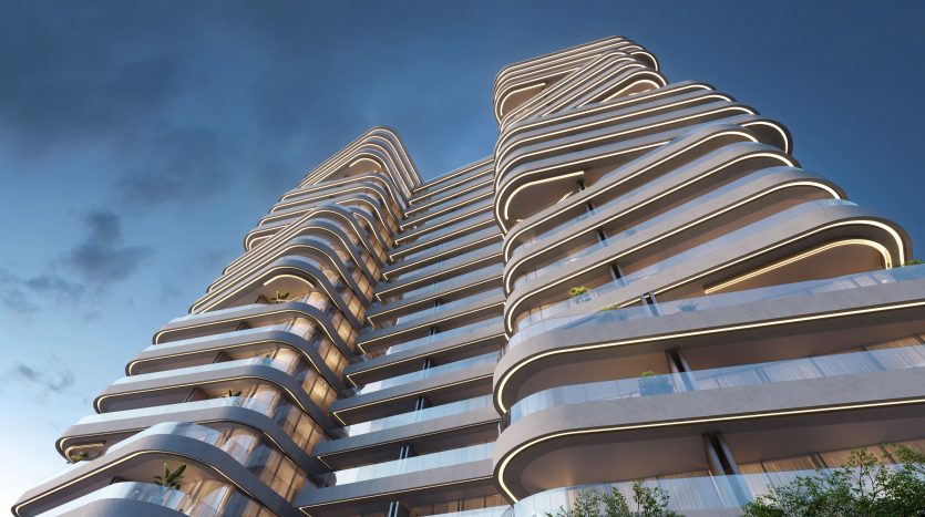 Immeuble de grande hauteur curviligne moderne avec balcons éclairés et plantes vertes luxuriantes, situé sur un ciel bleu clair au crépuscule à Dubaï.