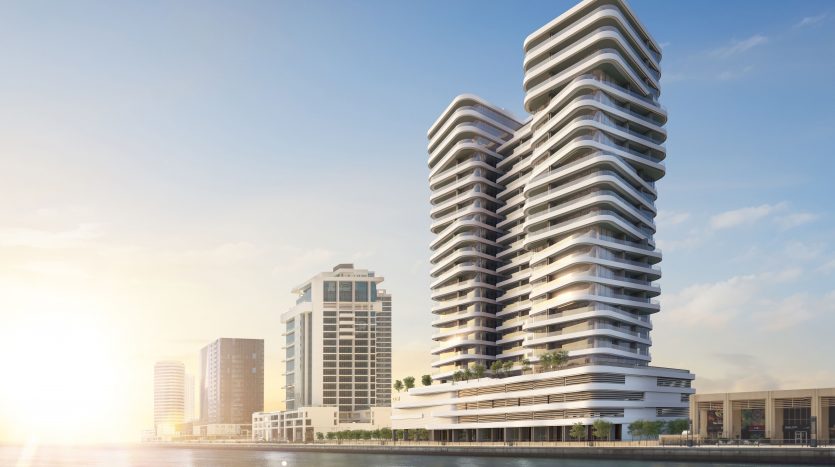 Bâtiments modernes en bord de mer à l&#039;architecture incurvée sous un ciel clair à Dubaï, reflétant le lever du soleil sur les eaux calmes.