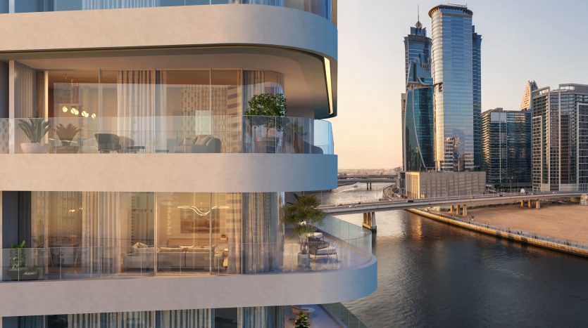 Vue extérieure d&#039;un bâtiment moderne à plusieurs étages avec des balcons incurvés, des intérieurs bien éclairés, sur un paysage urbain avec des tours de grande hauteur et une rivière au coucher du soleil à Dubaï.