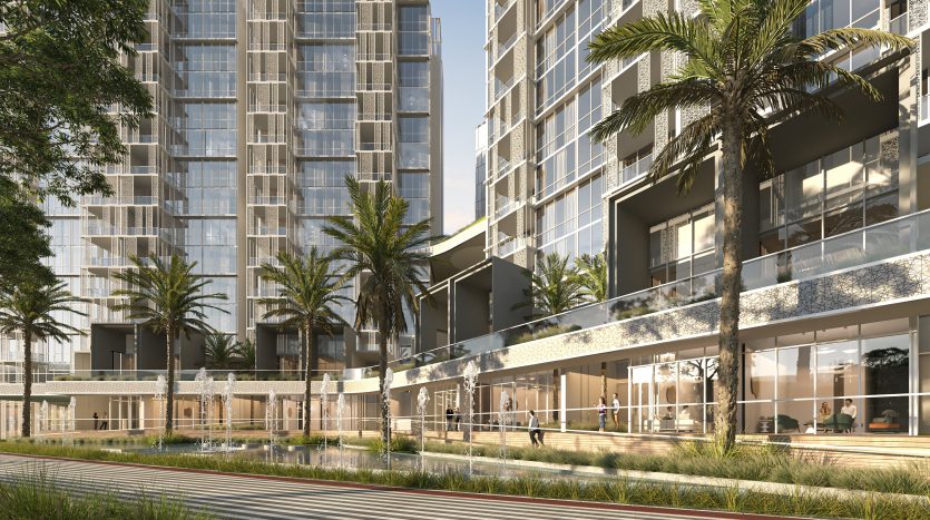 Un immeuble moderne de grande hauteur doté de vastes façades vitrées, entouré d'une verdure luxuriante et de palmiers à Dubaï. Les gens sont visibles en train de marcher et de se détendre dans le jardin structuré avec des balcons donnant sur la scène.