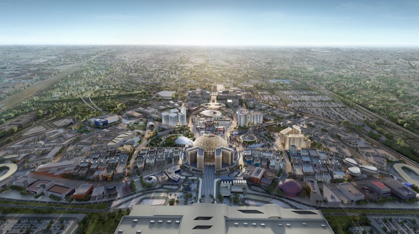 Vue aérienne d'un paysage urbain moderne présentant une structure centrale en forme de dôme entourée de divers bâtiments architecturaux, avec des routes complexes et une verdure luxuriante s'étendant vers l'horizon de Dubaï.