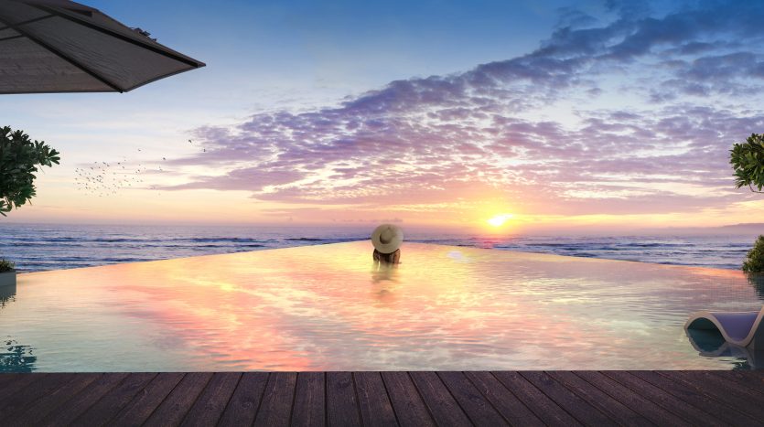Une personne portant un chapeau de soleil profite d&#039;un coucher de soleil serein depuis une piscine à débordement dans une villa à Dubaï, avec des oiseaux volant au loin et des plantes à proximité.