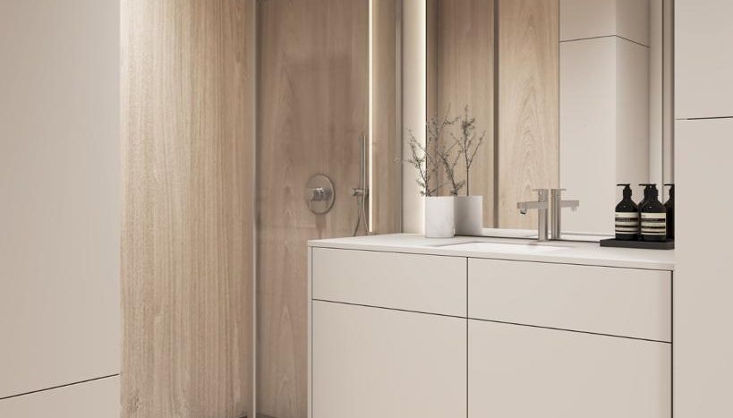 Une salle de bain moderne avec des armoires en bois, un lavabo blanc et une cabine de douche en verre. Le décor subtil comprend un vase de fleurs et des bouteilles noires minimalistes. Les tons clairs dominent l&#039;espace de cette villa Dubaï.
