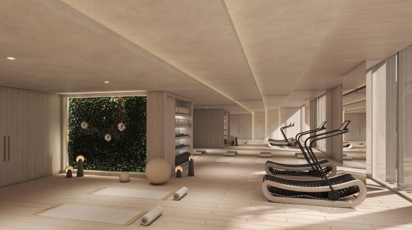 Intérieur de salle de sport moderne avec machines elliptiques, décoration minimaliste, panneaux en bois clair et grand mur végétal vert orné de fleurs. Éclairage doux et design spacieux idéal pour un appartement à Dubaï.
