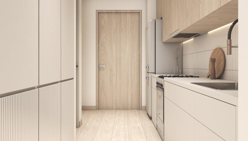 Une cuisine étroite et moderne dans une villa de Dubaï avec des armoires en bois clair et des comptoirs blancs, avec une cuisinière intégrée et une porte au bout. Les tons neutres et les éléments de design soignés donnent un aspect épuré et minimaliste.