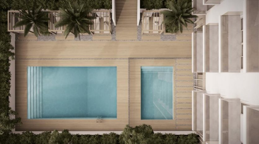 Vue aérienne d&#039;un projet architectural moderne à Dubaï comprenant deux grandes piscines bordées de palmiers et flanquées de bâtiments, reliées par un chemin sablonneux.