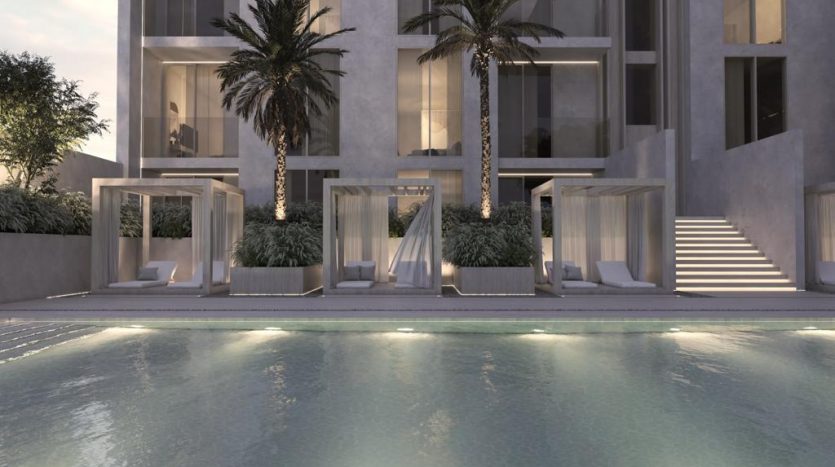 Maison à l&#039;architecture moderne comprenant une piscine au premier plan avec des cabanes éclairées et des palmiers sur fond d&#039;immeuble à plusieurs étages le soir, parfaite pour ceux qui s&#039;intéressent à l&#039;immobilier Dubaï.