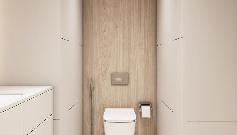 Une salle de bains moderne dans une villa à Dubaï comprenant des toilettes murales avec douchette de bidet, placées contre un panneau arrière en bois, flanquées de murs beiges doux et d&#039;une vasque blanche sur la gauche.