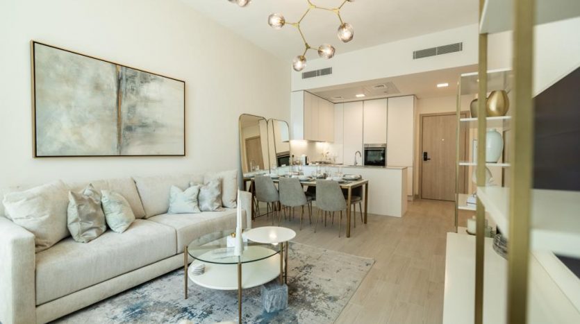 Un salon moderne dans une villa de Dubaï avec un canapé beige, des chaises assorties, une table basse ronde blanche et un grand tableau abstrait. La pièce s&#039;ouvre sur un coin repas avec une table dressée pour