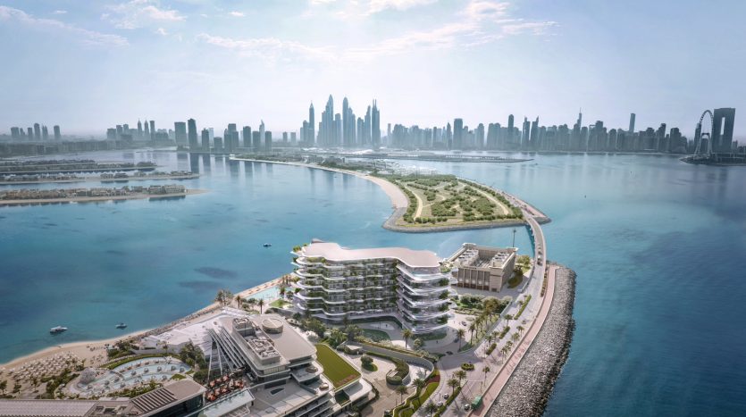Vue aérienne d&#039;un développement côtier moderne à Dubaï avec des bâtiments à plusieurs niveaux au design unique surplombant un lagon bleu, avec un horizon urbain en arrière-plan lointain sous un ciel clair.