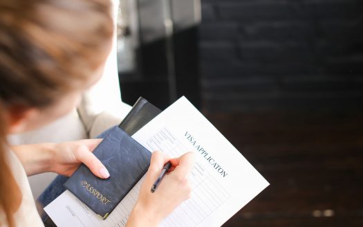 Une personne remplissant un formulaire de demande de visa avec un passeport en main, se concentrant sur le document posé sur une table en bois dans une villa de Dubaï.