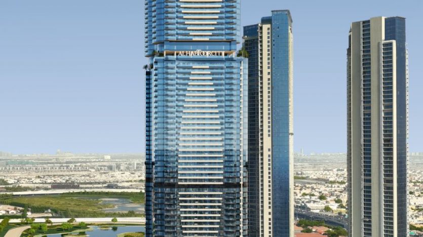 Vue aérienne d&#039;un grand gratte-ciel moderne avec une façade en verre bleu et des bandes horizontales distinctives, situé à côté d&#039;une autoroute très fréquentée et entouré d&#039;autres immeubles de grande hauteur à Dubaï.