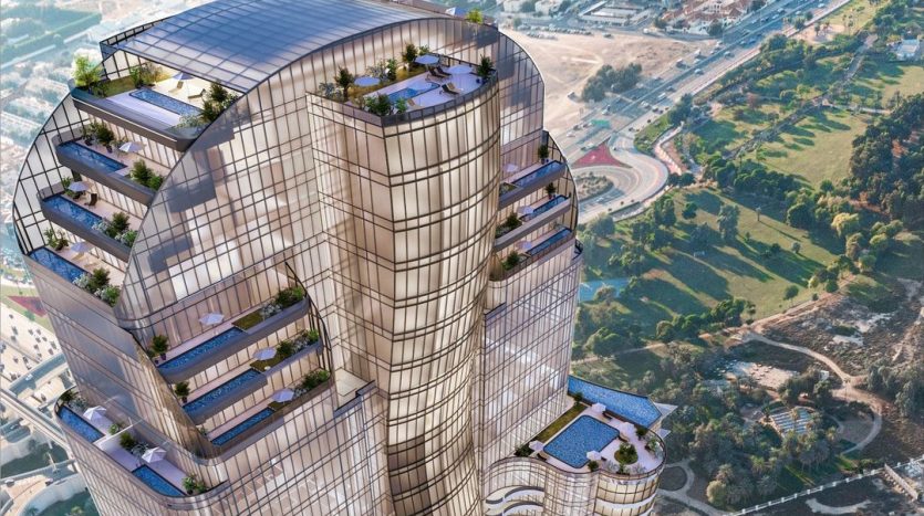 Vue aérienne d&#039;un gratte-ciel moderne à plusieurs niveaux avec des façades en verre et de multiples terrasses vertes à Dubaï, entouré d&#039;un paysage urbain et d&#039;espaces verts.
