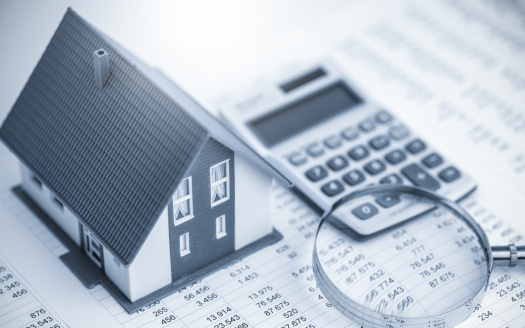 Un petit modèle de villa placé sur des documents financiers à côté d'une calculatrice et d'une loupe, représentant l'investissement et l'analyse immobiliers à Dubaï. L'image est dans des tons bleus monochromes.