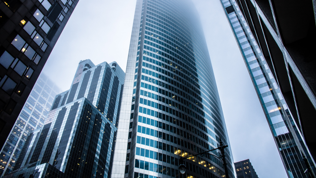 View from street level of towering skyscrapers under cloudy skies, with one building reflecting the overcast atmosphere well, surrounded by other high-rise structures ideal for investing in Dubai.