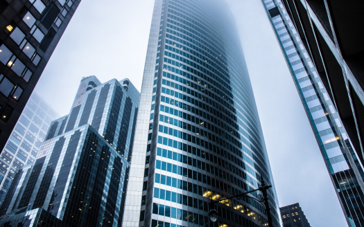 Vue depuis le niveau de la rue des gratte-ciel imposants sous un ciel nuageux, avec un bâtiment reflétant bien l'atmosphère couverte, entouré d'autres structures de grande hauteur idéales pour investir à Dubaï.