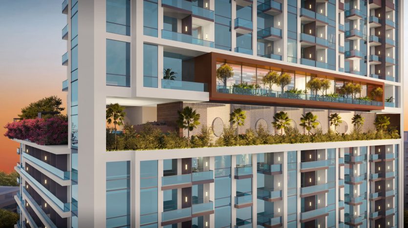 Immeuble d&#039;appartements moderne à Dubaï au crépuscule présentant des balcons en verre et des jardins en terrasse verdoyants contre un ciel coucher de soleil.