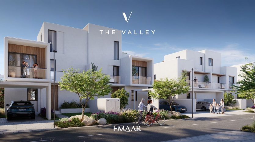 Rendu numérique d&#039;un quartier résidentiel moderne de Dubaï avec des maisons de ville blanches contemporaines, mettant en vedette des personnes en interaction et des véhicules garés. Le logo de « emaar the valley » est affiché en haut.