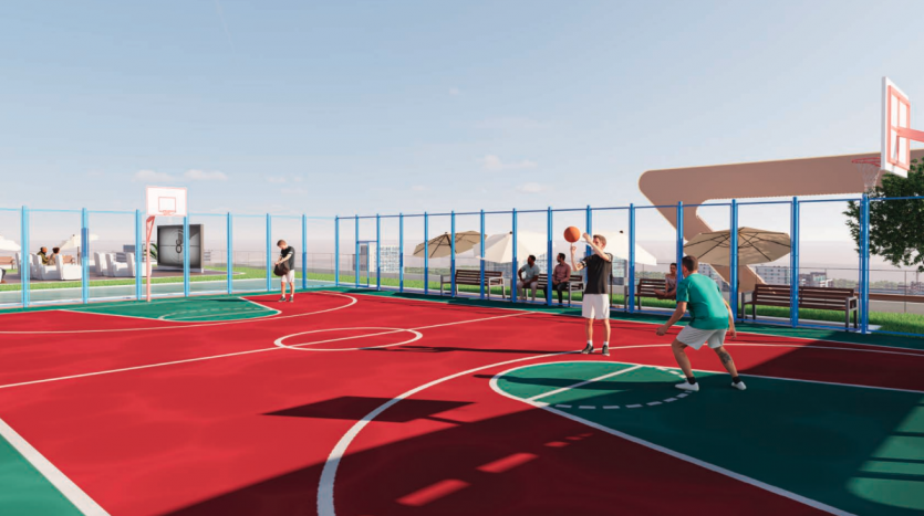 Terrain de basket extérieur avec joueurs participant à un match. Le terrain, situé à proximité d'une agence immobilière Dubaï, présente des zones rouges et vertes clairement délimitées sous un ciel ensoleillé. Certains joueurs tirent aux cerceaux pendant
