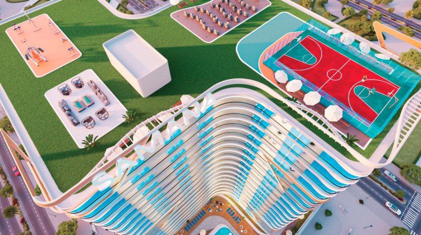 Vue aérienne d'un immeuble de grande hauteur moderne et incurvé avec des installations sportives telles que des courts de basket-ball et de tennis sur le toit entouré d'une verdure luxuriante et de routes adjacentes, mise en valeur par une agence immobilière de Dubaï.