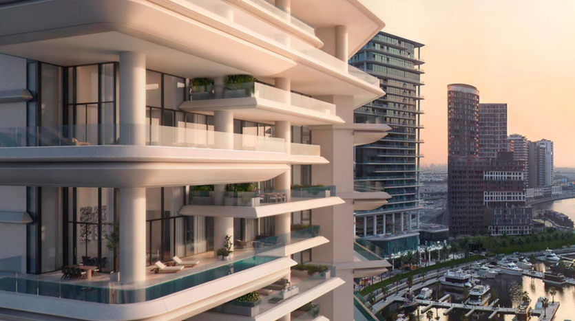 Un complexe d&#039;appartements moderne en bord de rivière à Dubaï, doté de balcons superposés, surplombe un paysage urbain au coucher du soleil, présentant un mélange de styles architecturaux et une marina avec des bateaux.