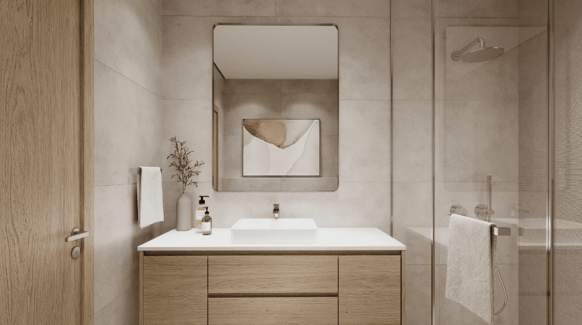 Intérieur de salle de bains moderne dans un appartement de Dubaï comprenant une vanité en bois avec un lavabo blanc, un miroir carré au-dessus et des carreaux beiges. Une serviette soigneusement suspendue et des accessoires muraux ajoutent à l&#039;ambiance épurée et minimaliste.