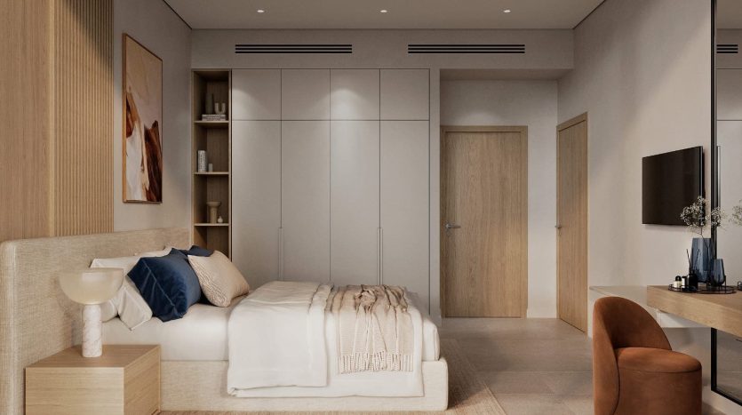 Chambre minimaliste dans un appartement de Dubaï avec un lit bas, des oreillers beiges et bleus, un banc en bois, une grande armoire et un fauteuil. Les tons neutres dominent l&#039;espace.