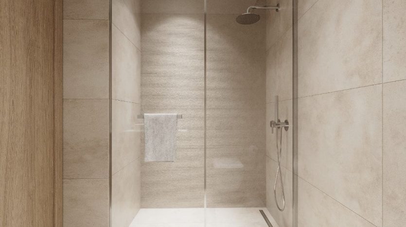Une salle de bain moderne dotée d&#039;une douche à l&#039;italienne entourée de verre, idéale pour l&#039;immobilier Dubaï, avec du carrelage beige clair aux murs et au sol, et une grande pomme de douche fixée au plafond.