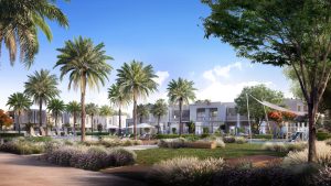 Une communauté résidentielle moderne de Dubaï comprenant des bâtiments blancs de faible hauteur entourés de palmiers luxuriants, des jardins paysagers avec des fleurs violettes et une aire de jeux, sous un ciel bleu clair.