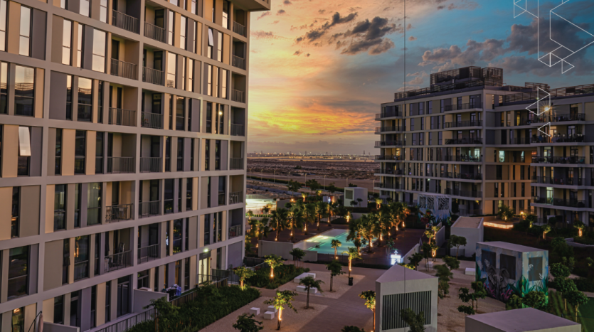 Une vue entre des immeubles modernes de grande hauteur au crépuscule, surplombant une cour soigneusement aménagée et un paysage urbain lointain sous un ciel de coucher de soleil vibrant à Dubaï.