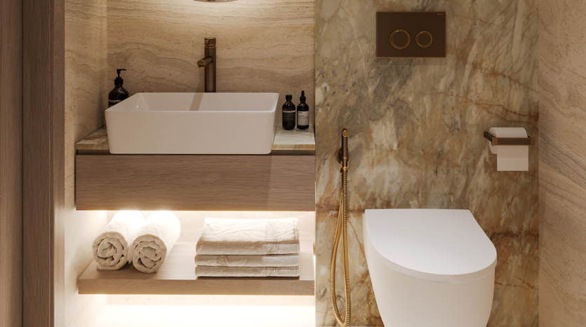 Salle de bains luxueuse dans une villa de Dubaï comprenant un lavabo rectangulaire blanc sur une vanité en bois, des murs en marbre et des luminaires dorés. Des toilettes blanches et des serviettes soigneusement pliées sur des étagères ajoutent au décor élégant