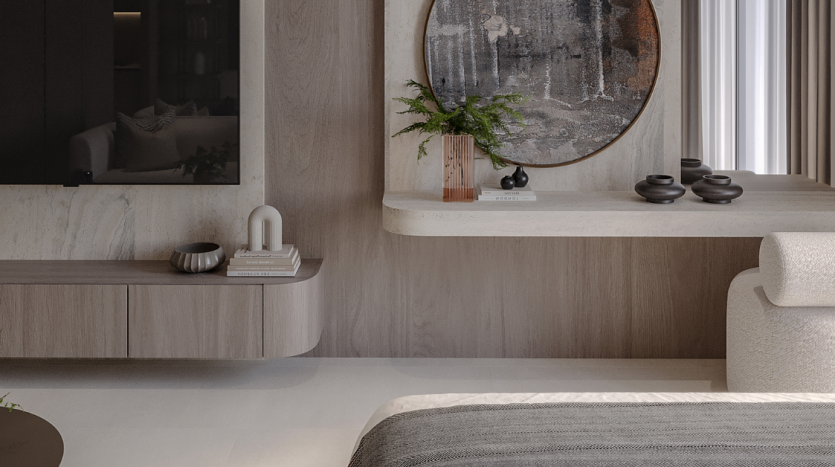 Une chambre minimaliste dans une villa de Dubaï comprenant une vanité en bois avec un miroir rond, des objets décoratifs et une chaise texturée moderne à côté d'un lit avec une couverture grise. La lumière naturelle filtre à travers des rideaux transparents.
