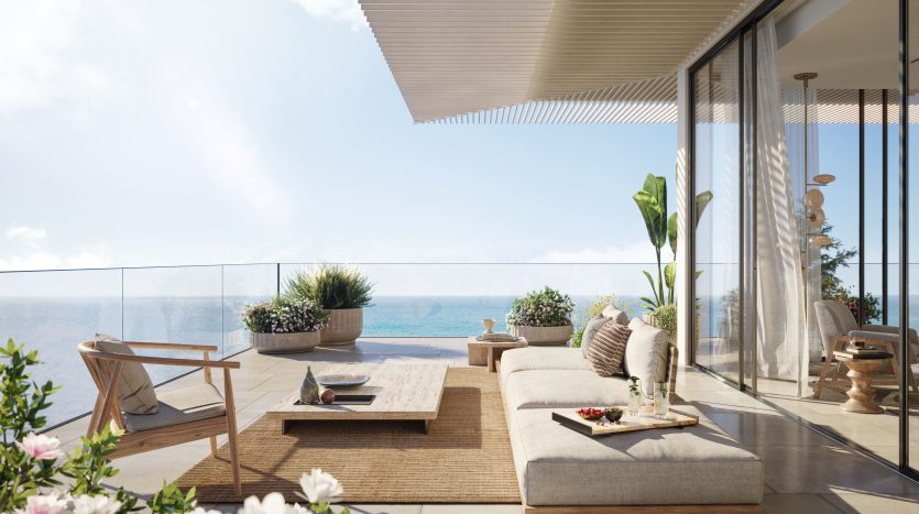 Un patio luxueux dans une villa de Dubaï doté d'un mobilier moderne avec vue sur l'océan, de sièges moelleux, de plantes décoratives et de portes vitrées allant du sol au plafond menant à l'intérieur.