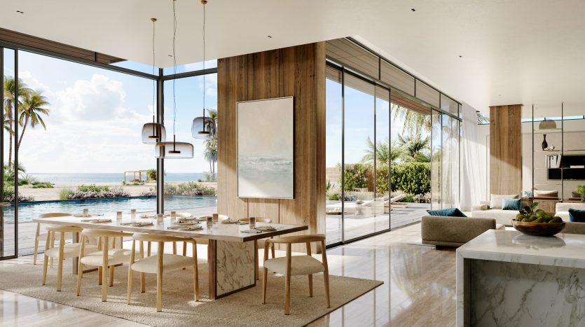 Salon et salle à manger décloisonnés modernes avec de grandes fenêtres vitrées offrant une vue panoramique sur une plage sereine et un ciel dégagé, caractéristiques des appartements de luxe à Dubaï. L'intérieur est conçu avec un mélange de bois