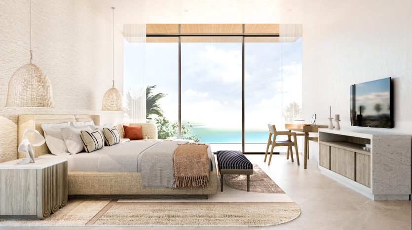 Une chambre lumineuse et moderne en bord de mer dans un appartement de Dubaï avec un grand lit, des lampes suspendues en rotin et une vue dégagée sur l'océan à travers des baies vitrées. Un petit coin salon et TV