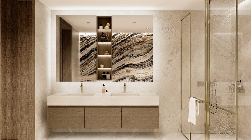 Une salle de bains luxueuse dans un appartement à Dubaï, comprenant une grande vasque avec deux lavabos, des armoires en bois et un mur en pierre texturée. Il y a une cabine de douche en verre à droite.