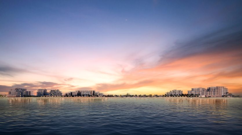 Un paysage urbain serein au bord de l'eau au coucher du soleil, avec des nuages orange et rose vibrants se reflétant dans les eaux calmes et des silhouettes de bâtiments modernes bordant l'horizon à Dubaï.