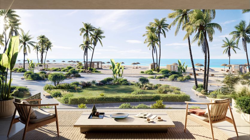 Vue depuis un luxueux patio en bord de mer avec deux chaises donnant sur un jardin paysager, une plage de sable fin, des palmiers et un ciel bleu clair à Dubaï.