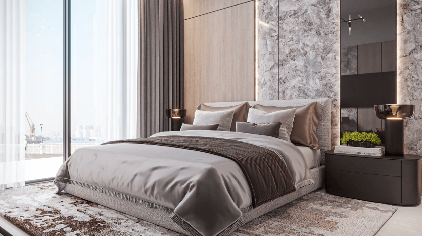 Chambre luxueuse dans un appartement de Dubaï comprenant un grand lit avec une literie grise moelleuse, flanqué de tables de nuit dorées. La pièce présente des murs en marbre, des panneaux en bois et une grande fenêtre donnant sur un paysage urbain.