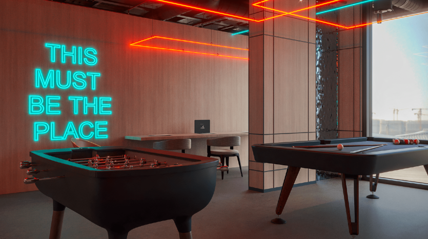 Salle de loisirs moderne avec des néons affichant &quot;This must be the place&quot;, comprenant un baby-foot, une table de billard et un bureau avec un ordinateur dans un appartement de Dubaï.