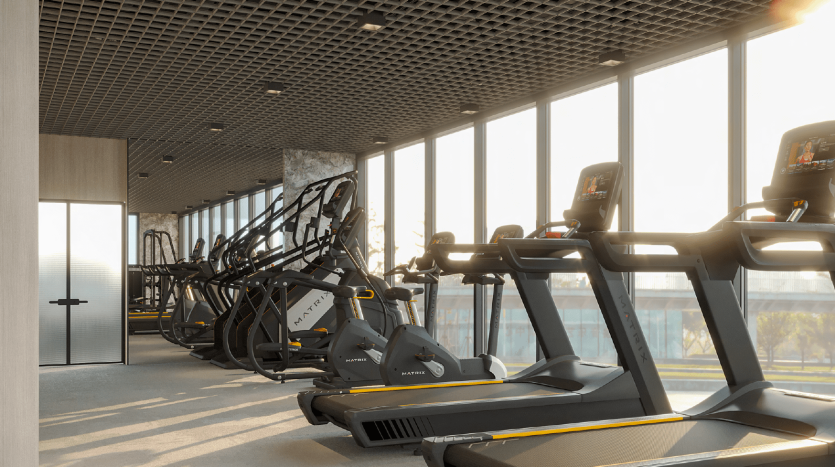 Salle de sport moderne avec des rangées de tapis roulants et de machines elliptiques faisant face à de grandes fenêtres offrant une vue sur le lever du soleil à Dubaï, créant une atmosphère d&#039;entraînement lumineuse et accueillante.