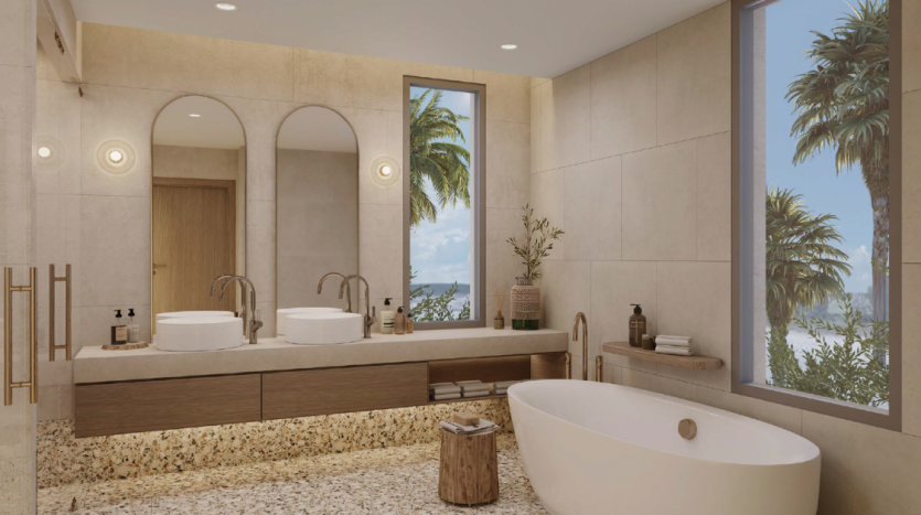 Une salle de bain luxueuse comprenant une baignoire autoportante, deux lavabos, des armoires en bois et une grande fenêtre avec vue tropicale. Le décor comprend des luminaires modernes et de la lumière naturelle, parfait pour un appartement
