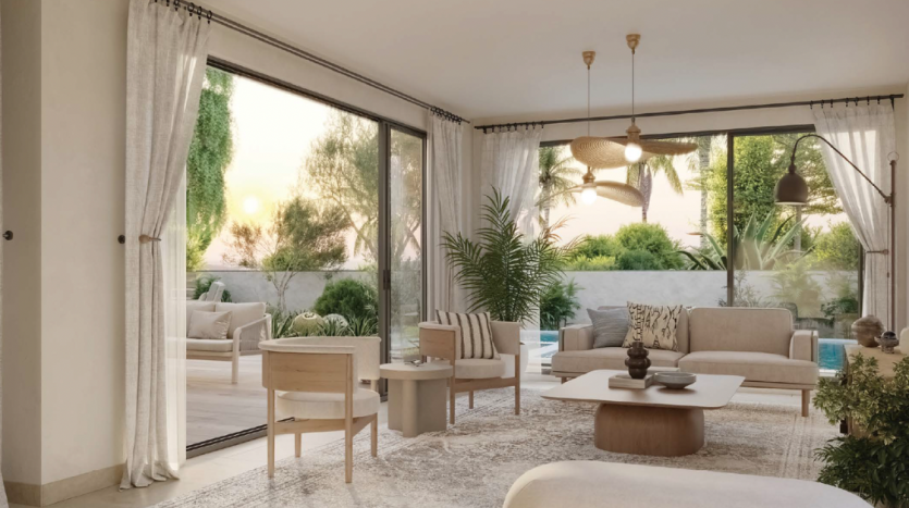 Un salon moderne dans une villa de Dubaï avec de grandes portes vitrées ouvertes sur un jardin, doté de meubles aux tons neutres, d&#039;un grand tapis et d&#039;un ventilateur de plafond, baigné de lumière chaude.