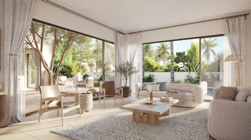 Un salon serein dans un appartement de Dubaï s&#039;ouvre sur un patio-jardin ensoleillé, doté de meubles beiges confortables, d&#039;un tapis neutre et de grandes fenêtres qui mettent en valeur la verdure luxuriante à l&#039;extérieur.