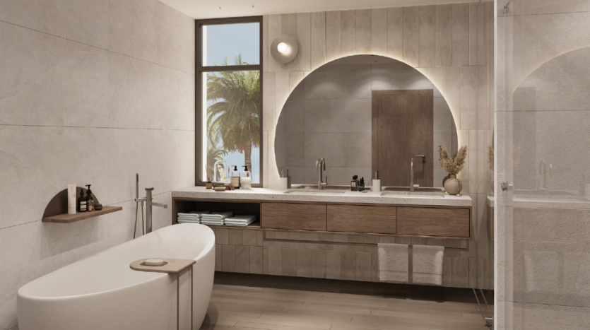 Salle de bain moderne avec un grand miroir au dessus d&#039;une vasque en bois, une baignoire autoportante et une cabine de douche. Une fenêtre révèle des palmiers à l&#039;extérieur, mélangeant les éléments intérieurs et extérieurs dans cet immobilier recherché