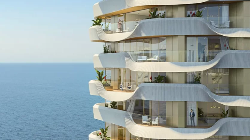 Immeuble moderne de plusieurs étages en bord de mer à Dubaï avec des balcons ondulés, des plantes luxuriantes et des personnes profitant de la vue.