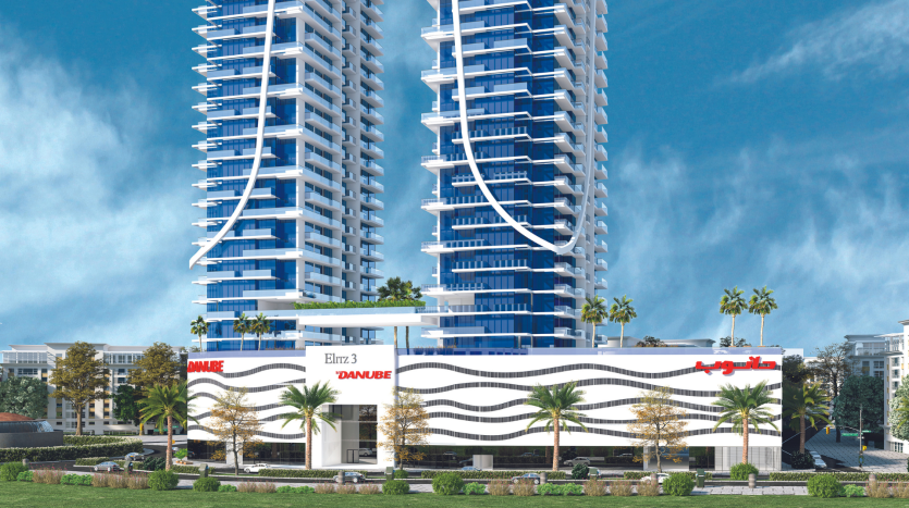Un immeuble résidentiel moderne de grande hauteur avec des balcons blancs incurvés compensés par du verre bleu sous un ciel clair, entouré d&#039;un aménagement paysager vert et doté d&#039;une *agence immobilière Dubaï* à la base