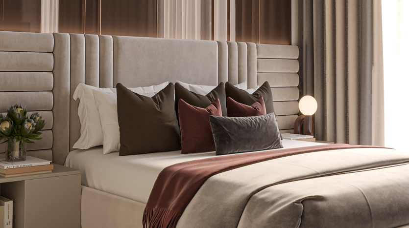 Une chambre luxueuse dans une villa de Dubaï comprenant un grand lit avec une tête de lit haute et rembourrée, recouverte d&#039;oreillers blancs, beiges et rouge foncé. Une table de chevet contient une lampe et un vase avec