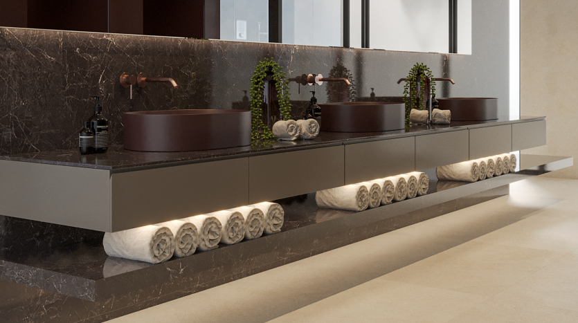 Un meuble-lavabo moderne avec des vasques marron foncé sur un comptoir en marbre, des serviettes blanches soigneusement roulées rangées en dessous et de petites plantes vertes comme décorations dans un luxueux appartement de Dubaï.